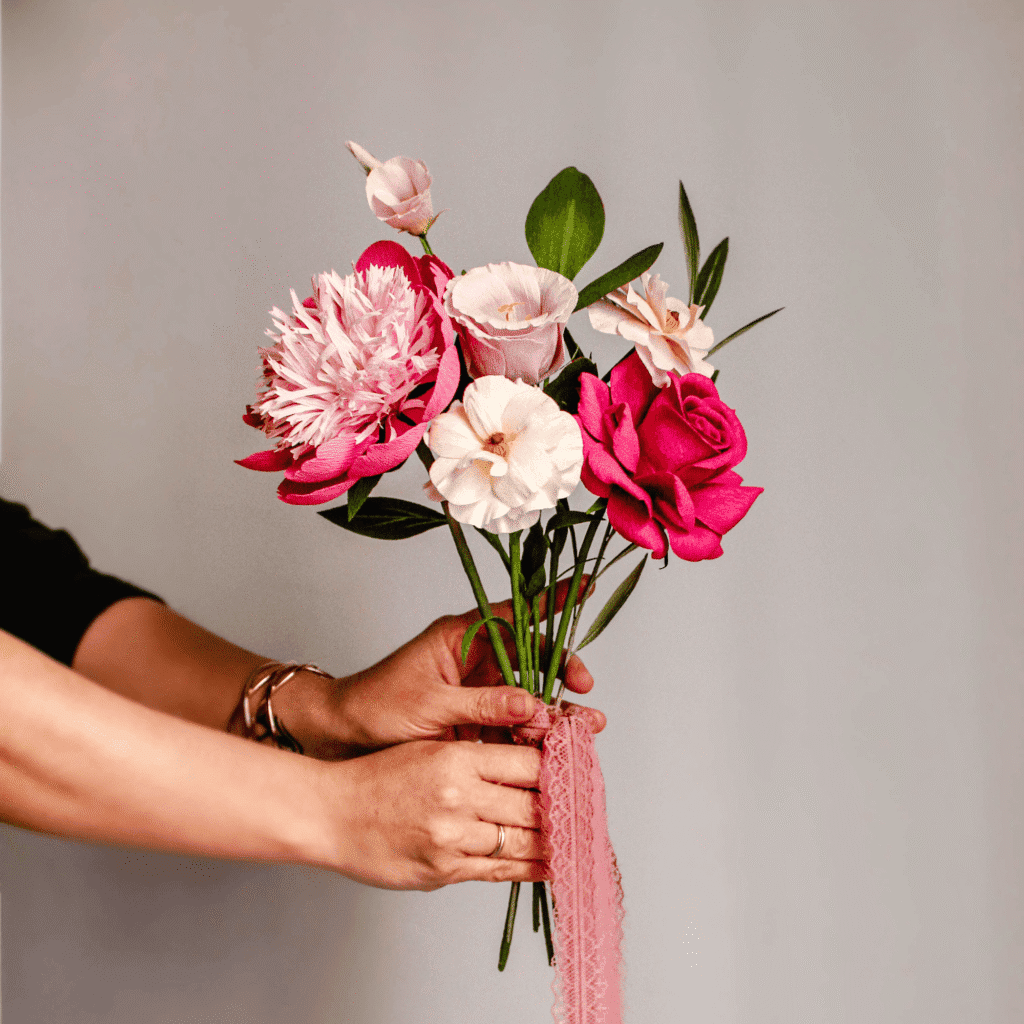 ramo de flores de papel crepé hecho a mano en tonos rosa y blanco sostenido con cinta rosa