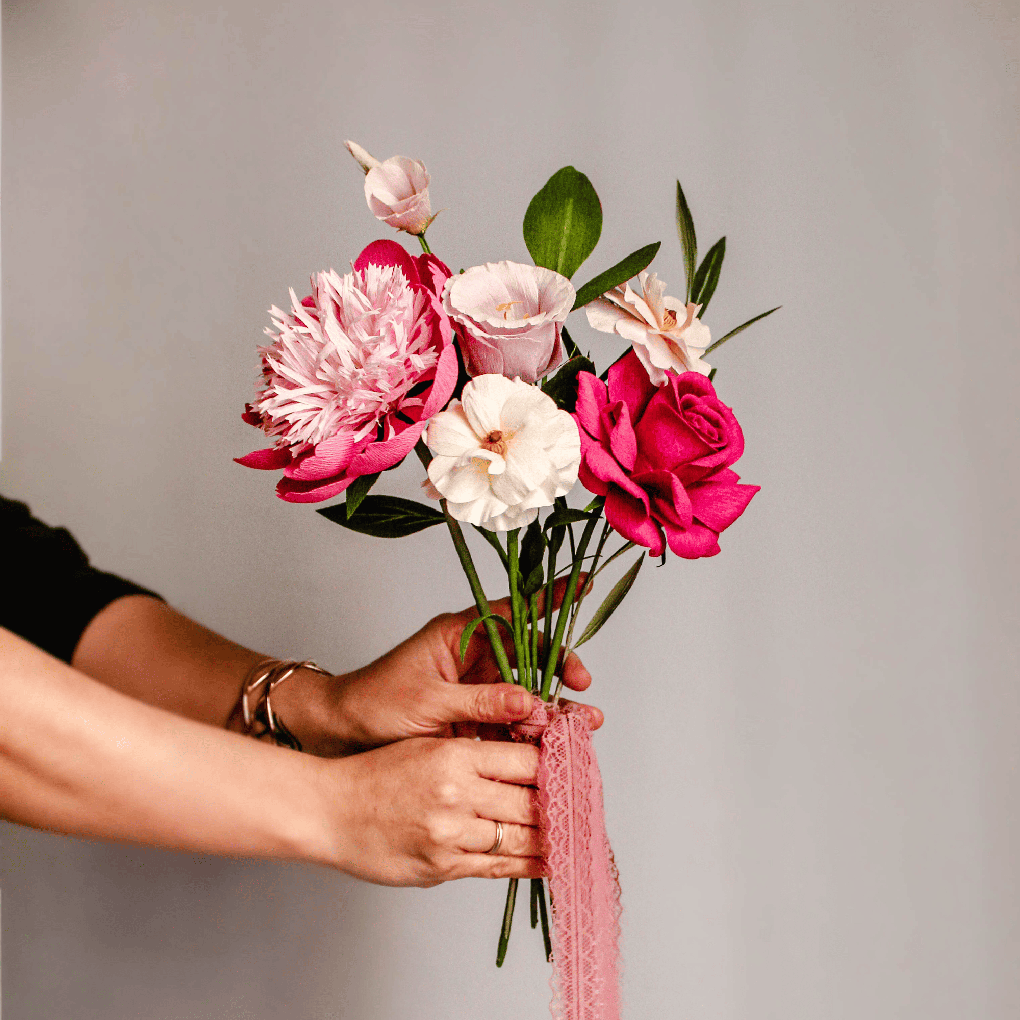 ramo de flores de papel crepé hecho a mano en tonos rosa y blanco sostenido con cinta rosa